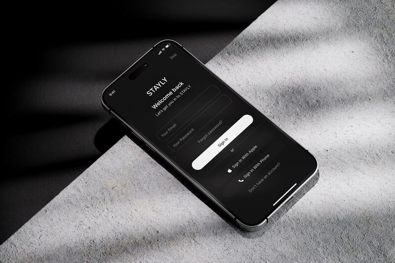 Экран входа в приложение STAYLY на iPhone, лежащем на краю бетонной плиты