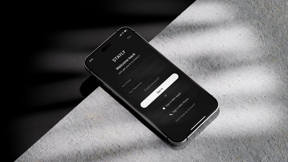 iPhone с экраном входа STAYLY лежит на бетонной плите в резкой тени от жалюзи